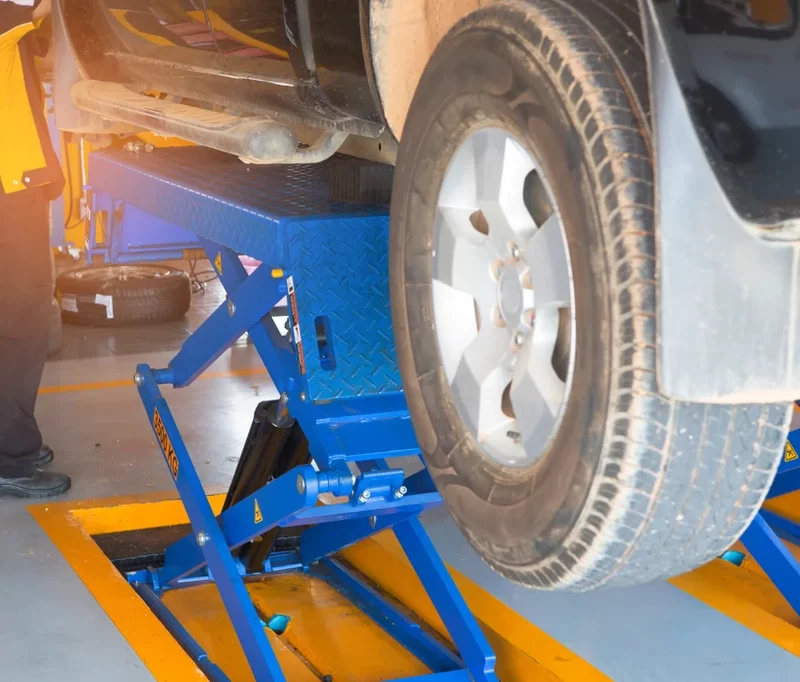 a mechanic working on a car that is lifted in the air by a blue car jack.